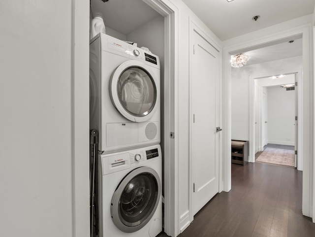 laundry room with a notable chandelier, dark wood-type flooring, and stacked washer and clothes dryer