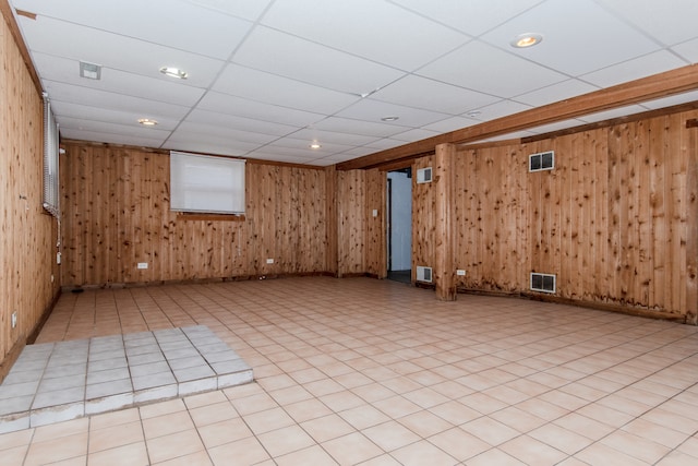 basement featuring a drop ceiling and wood walls