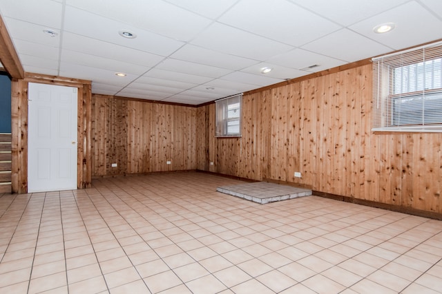 tiled empty room featuring wooden walls, a drop ceiling, and plenty of natural light