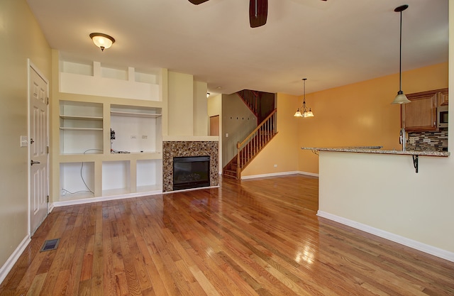 unfurnished living room featuring light hardwood / wood-style flooring, built in shelves, and ceiling fan with notable chandelier