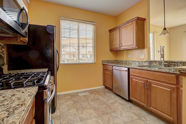 kitchen with appliances with stainless steel finishes, sink, decorative light fixtures, light stone counters, and light tile patterned floors