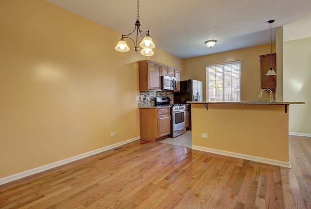 kitchen with a breakfast bar area, appliances with stainless steel finishes, an inviting chandelier, light hardwood / wood-style flooring, and decorative light fixtures