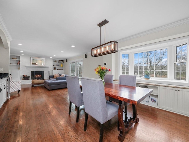 dining area with a brick fireplace, a healthy amount of sunlight, crown molding, and dark wood-type flooring