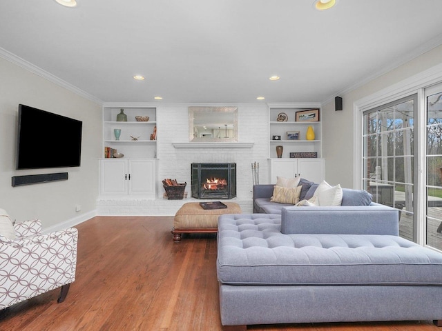 living room featuring wood-type flooring, a brick fireplace, built in shelves, and crown molding