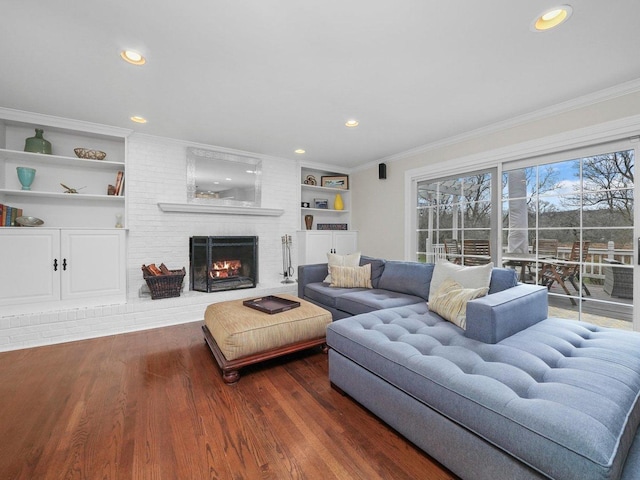 living room with built in shelves, dark hardwood / wood-style flooring, ornamental molding, and a fireplace