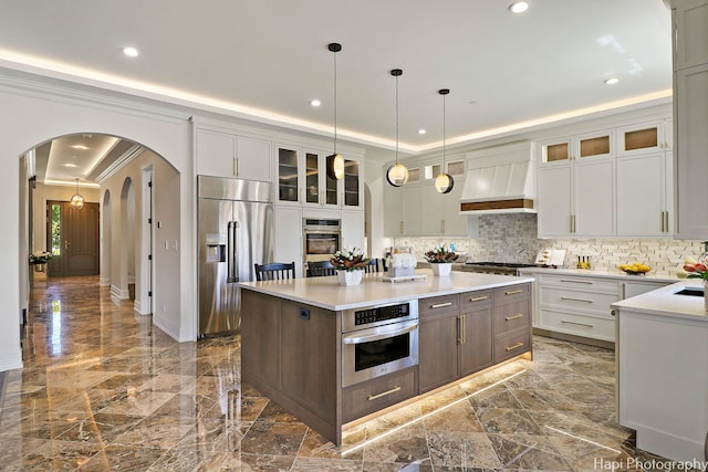 kitchen with appliances with stainless steel finishes, a kitchen island, pendant lighting, crown molding, and premium range hood