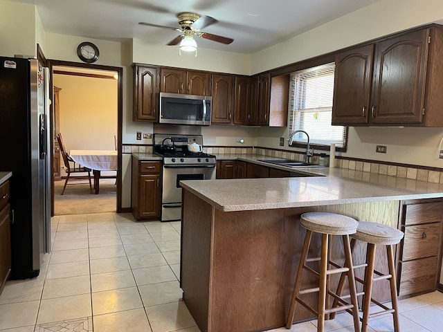 kitchen featuring sink, a kitchen bar, kitchen peninsula, ceiling fan, and stainless steel appliances