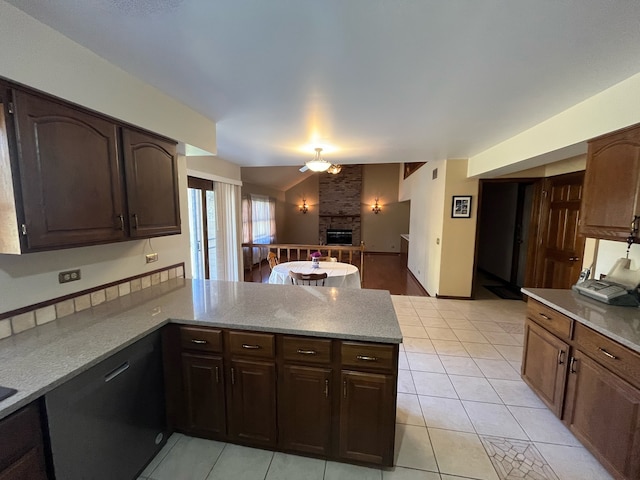 kitchen featuring a stone fireplace, kitchen peninsula, vaulted ceiling, light tile patterned flooring, and ceiling fan