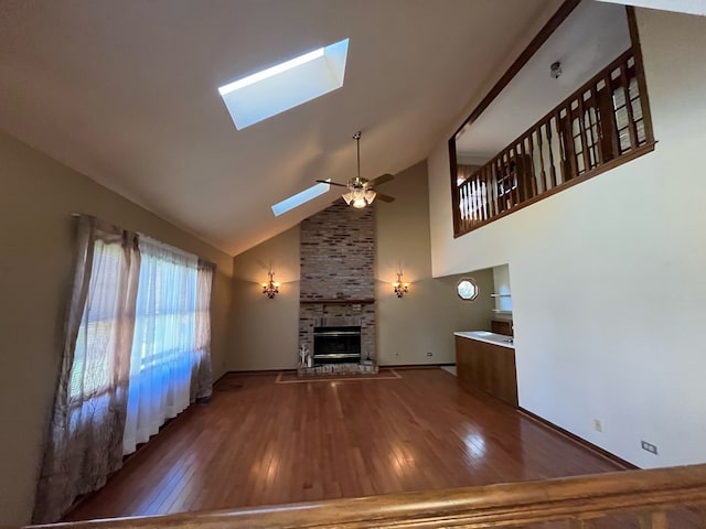 unfurnished living room featuring hardwood / wood-style flooring, a skylight, a fireplace, high vaulted ceiling, and ceiling fan