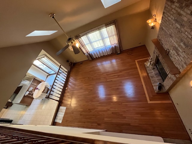 unfurnished living room with high vaulted ceiling, a skylight, a stone fireplace, ceiling fan, and hardwood / wood-style flooring