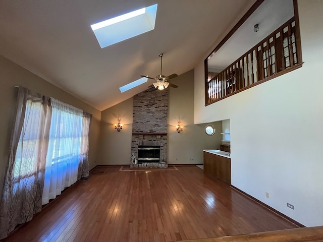 unfurnished living room featuring hardwood / wood-style flooring, a brick fireplace, a skylight, high vaulted ceiling, and ceiling fan