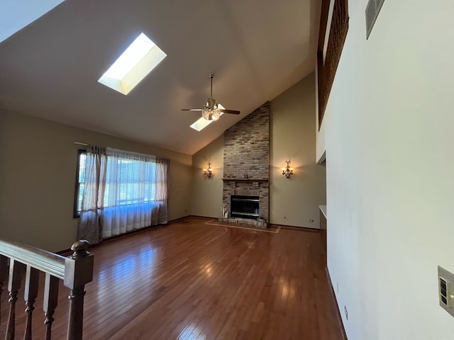 unfurnished living room with high vaulted ceiling, a skylight, a brick fireplace, ceiling fan, and hardwood / wood-style flooring