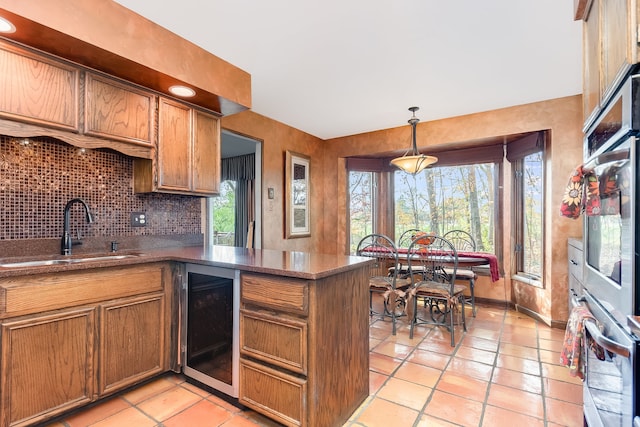 kitchen with sink, kitchen peninsula, hanging light fixtures, wine cooler, and decorative backsplash