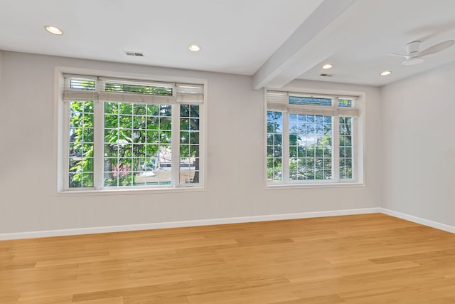 spare room with a healthy amount of sunlight, beamed ceiling, light wood-type flooring, and ceiling fan