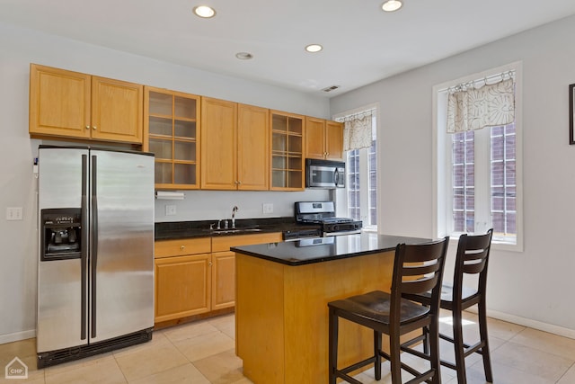 kitchen with a breakfast bar area, sink, a center island, light tile patterned flooring, and appliances with stainless steel finishes