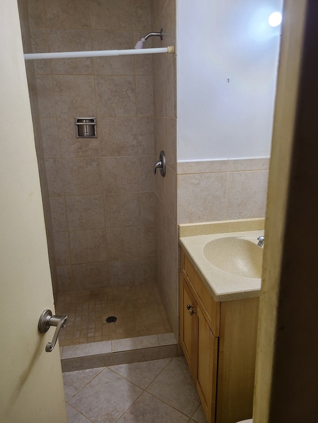 bathroom with tile walls, vanity, a tile shower, and tile patterned flooring