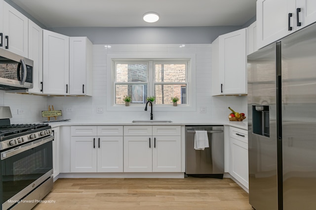 kitchen featuring decorative backsplash, appliances with stainless steel finishes, white cabinetry, light hardwood / wood-style flooring, and sink