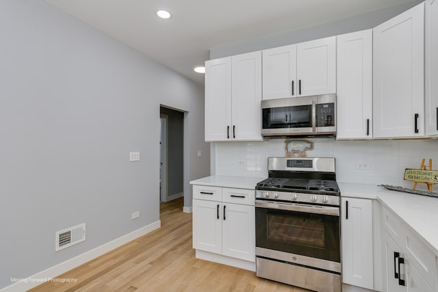 kitchen with stainless steel appliances, tasteful backsplash, light hardwood / wood-style flooring, and white cabinets