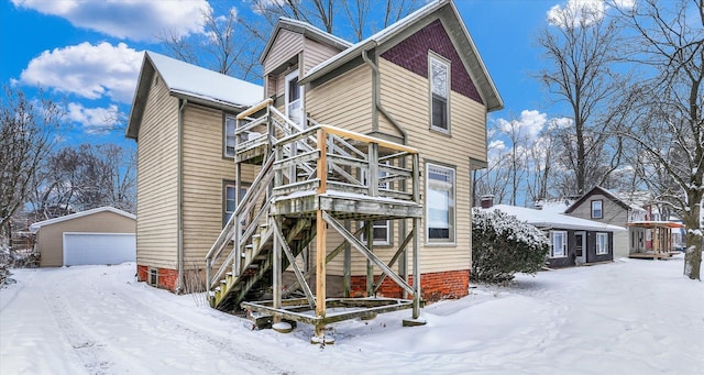 snow covered back of property with a garage, an outdoor structure, and a balcony