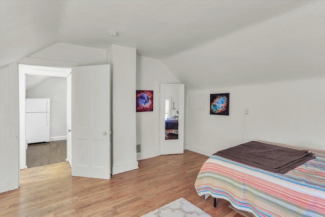 bedroom featuring lofted ceiling, light hardwood / wood-style flooring, and white refrigerator