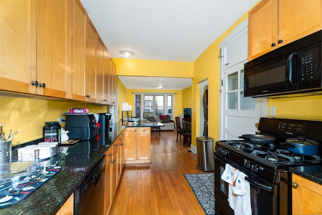 kitchen with dark stone counters, black appliances, light wood-type flooring, and ceiling fan