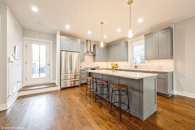 kitchen with a kitchen island, appliances with stainless steel finishes, dark hardwood / wood-style floors, pendant lighting, and wall chimney exhaust hood