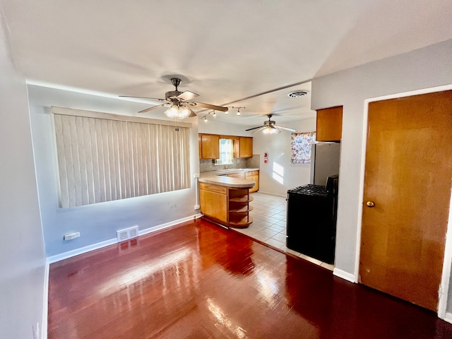 kitchen featuring dark hardwood / wood-style floors, kitchen peninsula, stainless steel fridge, tasteful backsplash, and ceiling fan