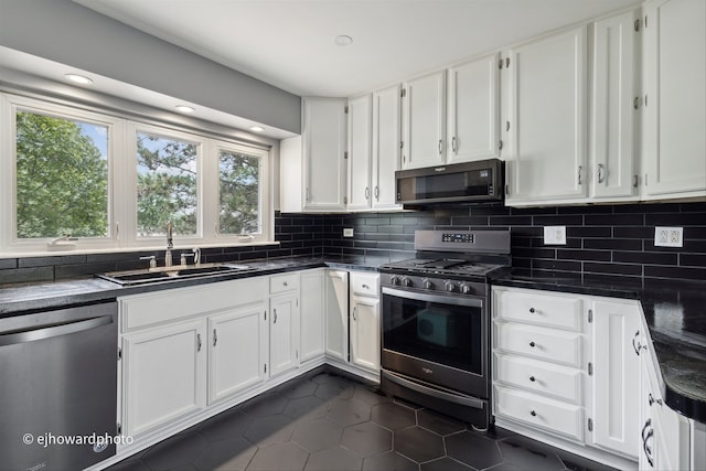 kitchen featuring tasteful backsplash, appliances with stainless steel finishes, white cabinetry, dark tile patterned flooring, and sink