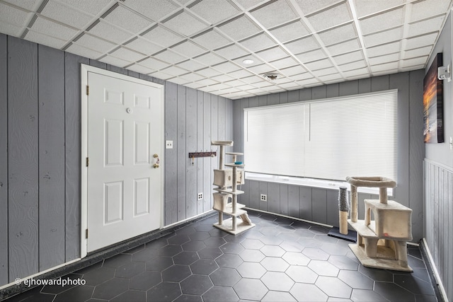 interior space with wooden walls, a paneled ceiling, and dark tile patterned flooring