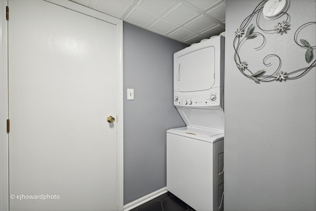 clothes washing area featuring stacked washer / dryer and dark tile patterned flooring