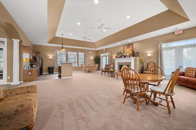 carpeted dining room with french doors, a tray ceiling, ornate columns, ceiling fan, and a tiled fireplace