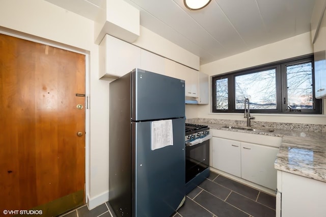 kitchen featuring stainless steel fridge, dark tile patterned floors, sink, black gas range, and white cabinetry