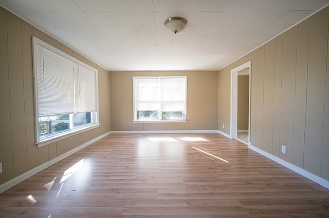 unfurnished room featuring a healthy amount of sunlight, light hardwood / wood-style flooring, and wooden walls