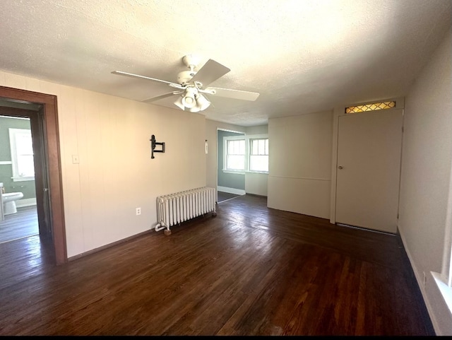 empty room featuring dark wood-type flooring, a textured ceiling, radiator, and ceiling fan