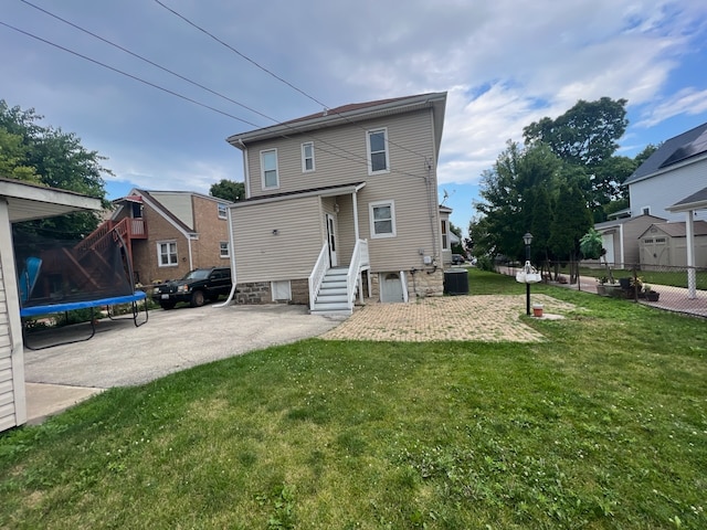 rear view of property with cooling unit, a yard, and a trampoline