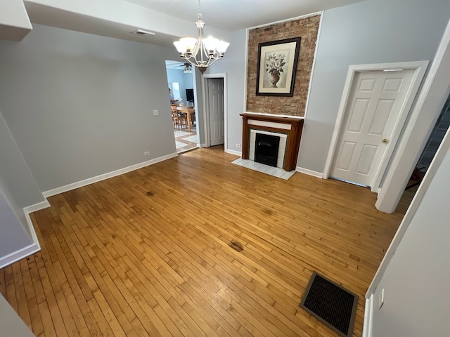 unfurnished living room featuring an inviting chandelier, a large fireplace, and light wood-type flooring