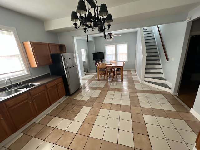 kitchen featuring light tile patterned flooring, stainless steel refrigerator, sink, and ceiling fan with notable chandelier