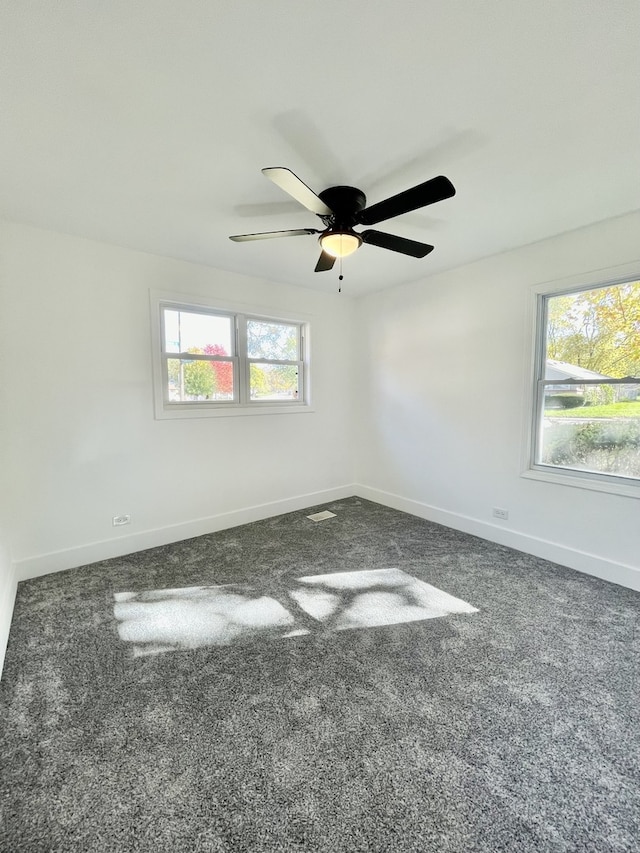 spare room featuring ceiling fan, plenty of natural light, and dark colored carpet