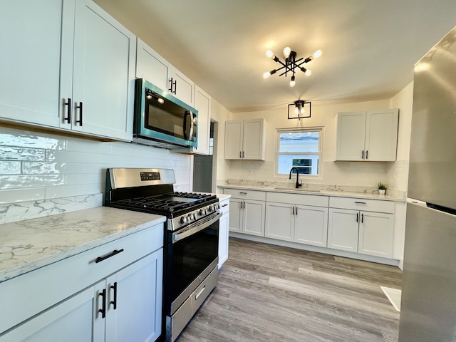 kitchen with stainless steel appliances, sink, light stone countertops, white cabinetry, and light hardwood / wood-style floors