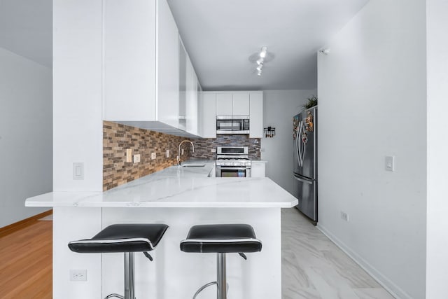 kitchen with kitchen peninsula, backsplash, a kitchen breakfast bar, white cabinetry, and stainless steel appliances