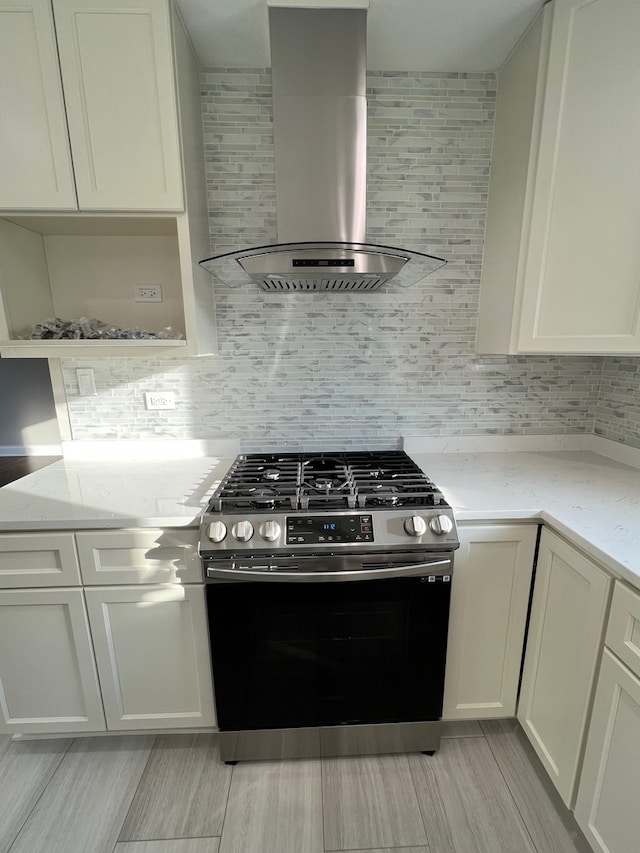 kitchen featuring wall chimney range hood, gas stove, white cabinets, backsplash, and light stone countertops