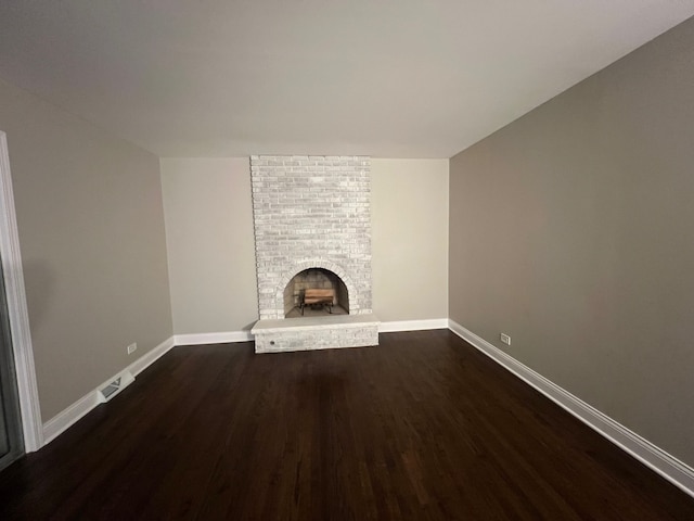 unfurnished living room with a brick fireplace and dark hardwood / wood-style floors