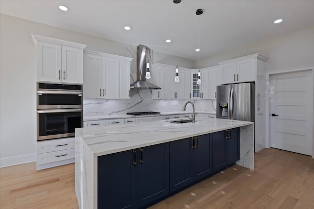 kitchen featuring wall chimney exhaust hood, hanging light fixtures, sink, white cabinets, and appliances with stainless steel finishes