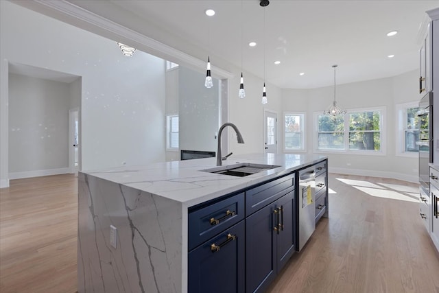 kitchen with light stone countertops, sink, light wood-type flooring, hanging light fixtures, and a center island with sink