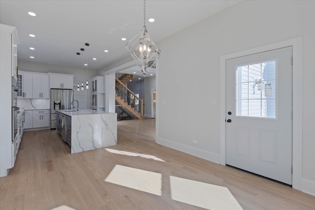 kitchen with white cabinetry, light hardwood / wood-style flooring, an island with sink, and hanging light fixtures