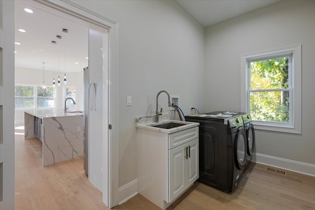 washroom featuring sink, washer and dryer, light hardwood / wood-style floors, and cabinets