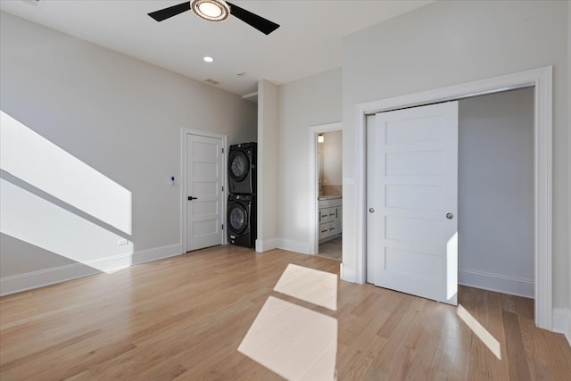 unfurnished bedroom featuring light hardwood / wood-style flooring, ensuite bath, stacked washer / dryer, and ceiling fan