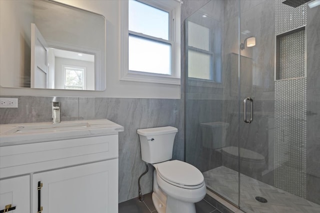 bathroom featuring toilet, walk in shower, vanity, and tile walls