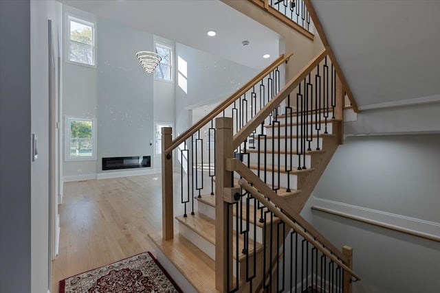 staircase featuring a towering ceiling, wood-type flooring, and an inviting chandelier