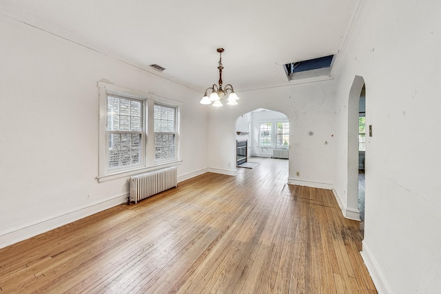 unfurnished dining area featuring a chandelier, radiator heating unit, and wood-type flooring